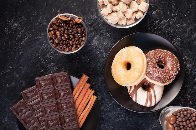 Draufsicht auf Schokoladentabletten, Donuts, brauner Zucker mit Erdnüssen in Schokolade und Kaffeebohnen auf dunklem Vintage-Holzhintergrund