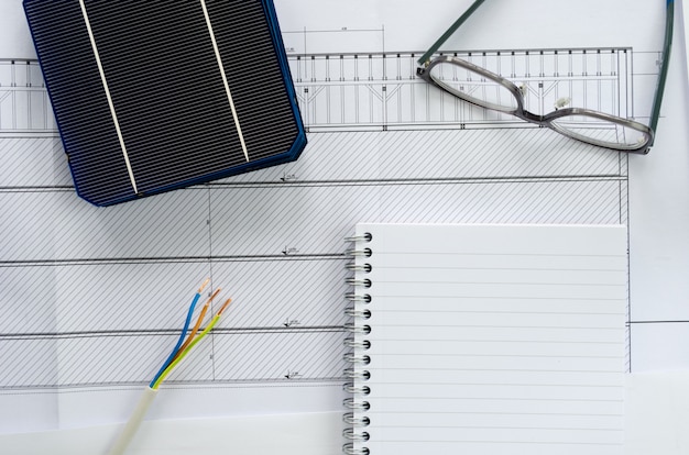 Draufsicht auf Solarzellen, Notizblock, Brille und Elektrokabel als Planungskonzept für ein Photovoltaikprojekt