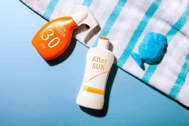 Draufsicht auf Sonnencreme und After-Sun-Lotion auf blauem Hintergrund mit einem Fischschimmel und einem Sommerpflegekonzept mit gestreiftem Handtuch