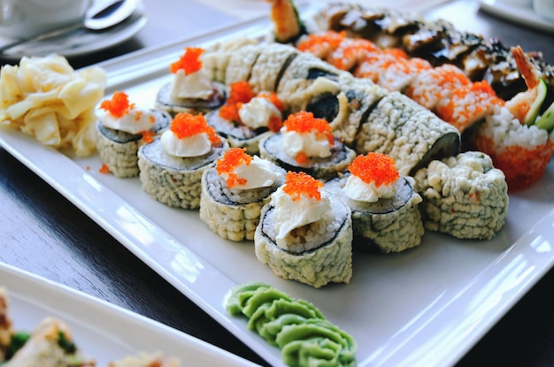 Draufsicht auf Sushi-Rollen mit Lachs, Aal, Gurke, Käse und Wasabi auf dem Teller im Restaurant
