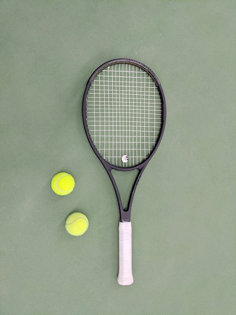 Draufsicht auf Tennisschläger und zwei Bälle auf dem grünen Sandtennisplatz.