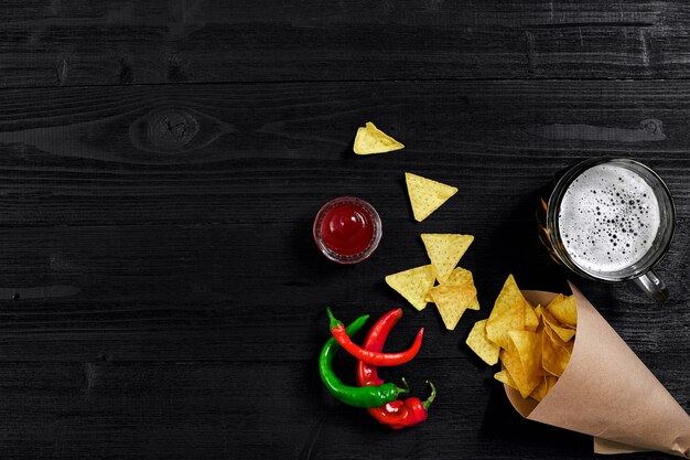 Draufsicht auf Tortilla-Chips mit Saucenglas Bier und rotem Chili auf schwarzem Holzhintergrund