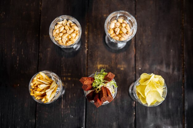 Draufsicht auf verschiedene salzige snacks der bierbar in gläsern auf dem dunklen holztisch