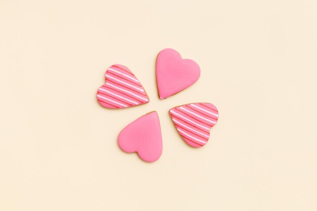 Draufsicht auf vier kleine rosa Lebkuchenplätzchen in Form von Herzen auf hellgelbem Hintergrund
