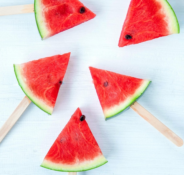 Draufsicht auf Wassermelonenscheiben-Eis am Stiel auf weißem Holzhintergrund