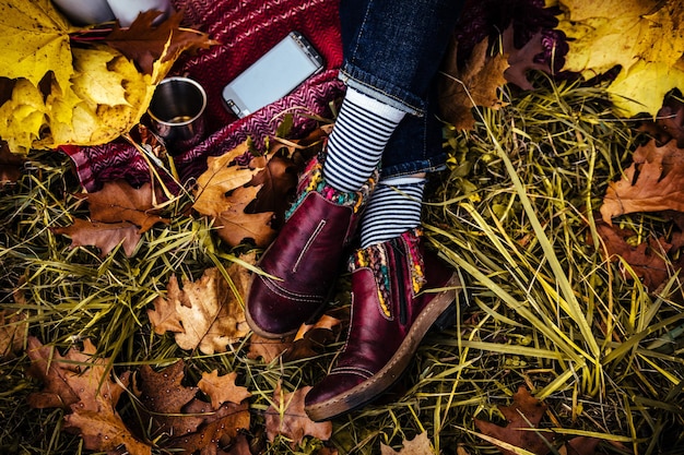 Draufsicht auf weibliche Beine in Jeans und braunen Schuhen auf einem Hintergrund gelber Herbstblätter