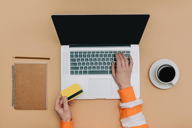 Draufsicht auf weibliche Kundenhände mit Karte und Laptop-Computer neben Notebook und Tasse Kaffee beim Kauf