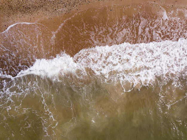 Draufsicht auf Wellen, die im Sand brechen und über tropische Sandstrände und Wellen fliegen