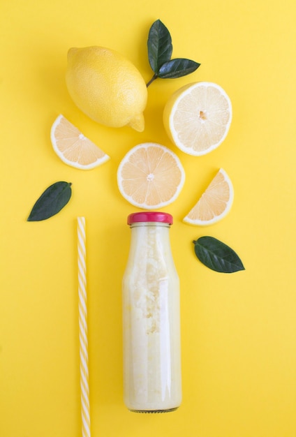 Draufsicht auf Zitronen-Smoothie in einer Glasflasche auf gelbem Hintergrund. Nahaufnahme.