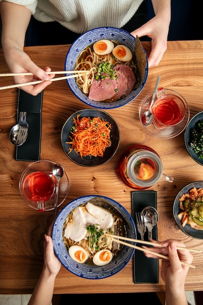 Draufsicht auf zwei Leute essen japanische Ramen-Nudelsuppen und andere asiatische Gerichte