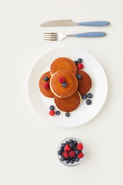 Draufsicht bei minimaler Zusammensetzung der köstlichen goldenen Pfannkuchen, die mit frischen Beeren neben Parfait-Tasse verziert werden, gesundes Frühstückskonzept