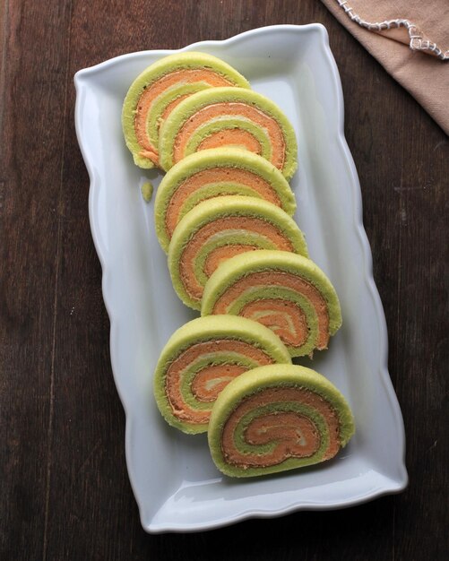 Draufsicht Bolu Gulung oder Roll Cake Pandan und Erdbeere mit Vanillecreme in Scheiben geschnitten serviert auf Holzhintergrund Kopierraum