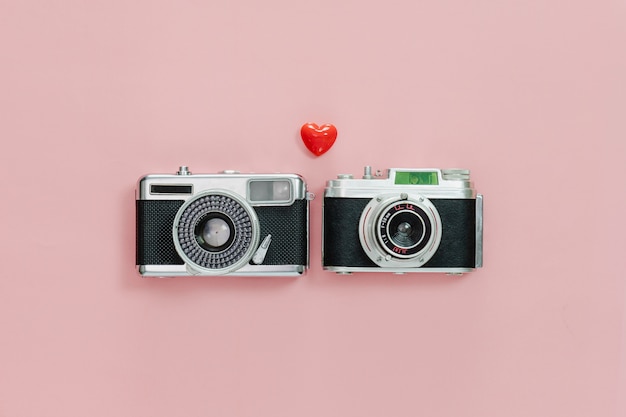 Draufsicht der alten Kamera der Weinlese und des kleinen roten Herzens auf rosa Pastellhintergrund.