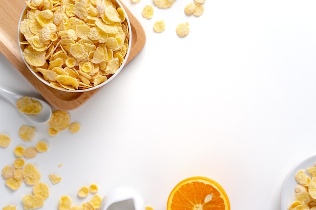 Draufsicht der Cornflakes-Schüssel-Süßigkeiten mit Milch und Orange auf weißem Hintergrund, flaches Überkopflayout, frisches und gesundes Frühstückskonzept.