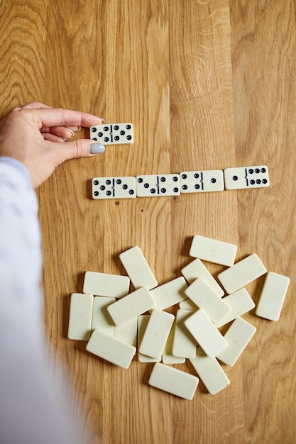 Draufsicht der Frauenhand spielen weiße Dominospiele auf Holztischhintergrund mit Kopienraum-Brettspielkonzept