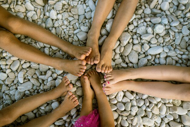 Draufsicht der Füße von fünf Kindern in einer Sternform am Kieselstrand