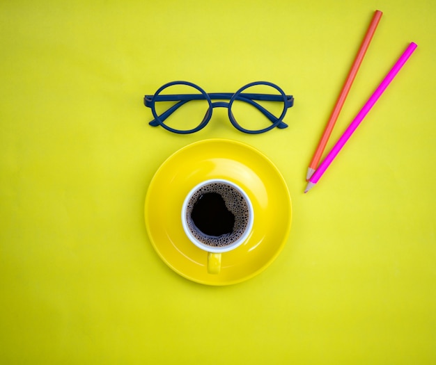 Draufsicht der gelben Kaffeetasse mit Lehrergläsern und buntem Bleistift auf gelbem Papierhintergrund