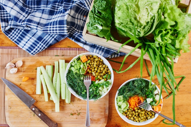 Draufsicht der Gemüsemischung in den Schüsseln mit grünen Erbsen, Gurken, Karotten, Kopfsalat und Dill