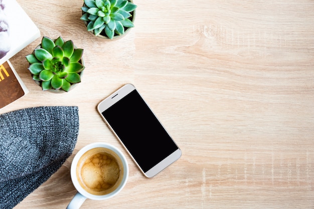 Draufsicht der gemütlichen Heimszene. Bücher, Wolldecke, Tasse Kaffee, Telefon und Sukkulenten über Holz. Speicherplatz kopieren, Modell.