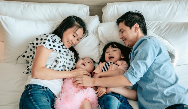Draufsicht der glücklichen Familie hat Spaß im Schlafzimmer Genießen Sie das Zusammensein Eltern kitzeln ihr kleines Baby, während sie im Bett liegenWochenendaktivität glückliches Familienlebensstilkonzept