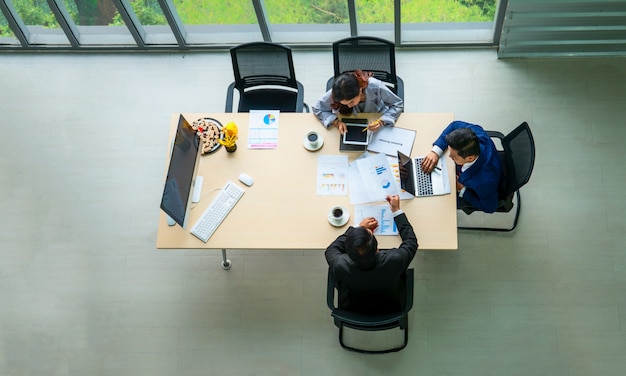 Draufsicht der Gruppe der multiethnischen beschäftigten Leute, die in einem Büro arbeiten, Luftaufnahme mit Geschäftsmann und Geschäftsfrau, die um einen Konferenztisch mit leerem Kopienraum sitzen, Geschäftstreffen