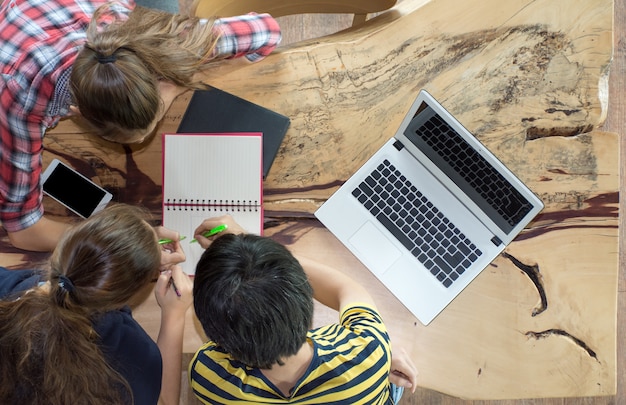 Draufsicht der Gruppe Kollegen, die im Team mit Berichten und Laptop auf Holztisch arbeiten