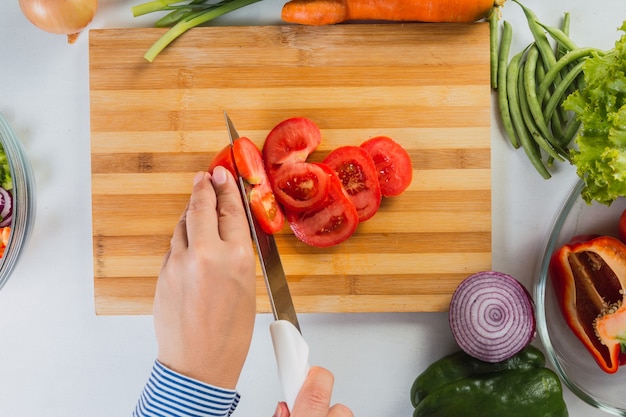 Draufsicht der Hände, die frische Tomaten schneiden.