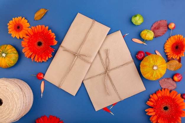 Draufsicht der handgemachten Geschenkbox mit gelben und orange Blumen und Kürbissen auf blauer Wand Leere Grußkarte für kreatives Arbeitsdesign. flach liegen