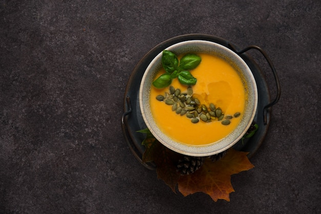 Draufsicht der heißen Herbstkürbissuppe mit Kürbiskernen auf dunklem strukturiertem Hintergrund