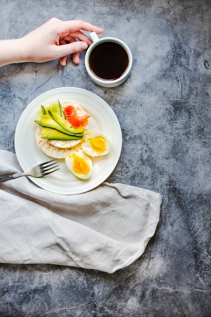 Draufsicht der jungen Frau, die eine Mittagspause hat. Knusprige Reiskuchen mit Avocado und frisch gesalzenem Lachs. Männliche Hände mit fett- und eiweißreicher Nahrung. Platz für Text.