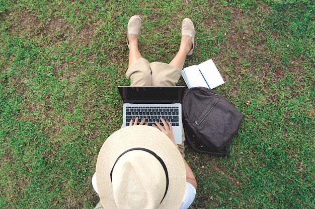 Foto draufsicht der jungen frau, die laptop beim sitzen im garten verwendet.