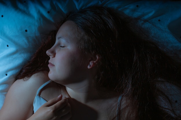 Draufsicht der jungen Frau, die nachts gemütlich auf einem Bett schläft, blaue Nachtfarben