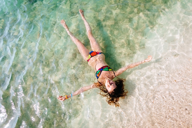 Draufsicht der jungen Frau in einem hellen Bikini schwimmt im transparenten, blauen Meer. Luftaufnahme der dünnen Frau liegend und auf das Wasser von Andamanensee schwimmend. Phuket, Thailand.