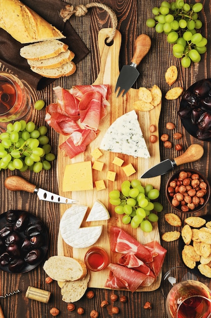 Draufsicht der Käseplatte mit Dorblu, Brie, Cheddar, Schinken, Trauben, Honig, Datteln, Crackern, Nüssen und Wein