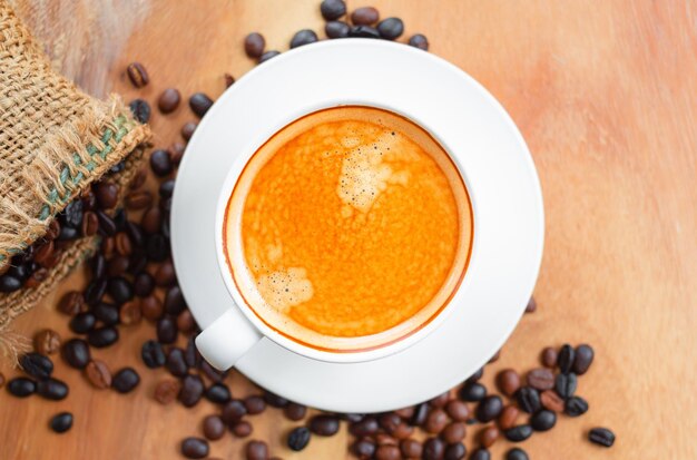 Draufsicht der Kaffeetasse hat goldenen Schaum und gemischte oder gemischte Kaffeebohnen in braunem Sack auf Holztisch