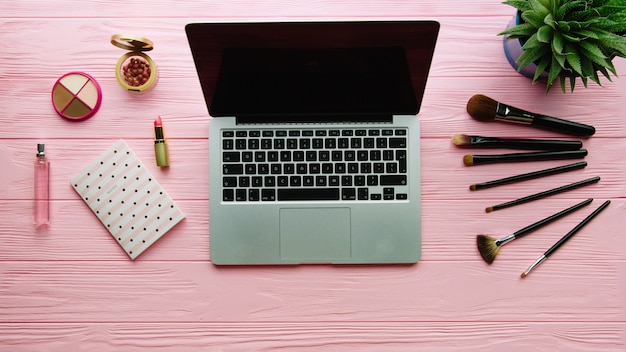 Draufsicht der kreativ dekorierten Komposition mit Kosmetik, Make-up-Werkzeugen, Zubehör und Laptop auf Farboberfläche. Beauty-, Mode-, Party- und Einkaufskonzept.