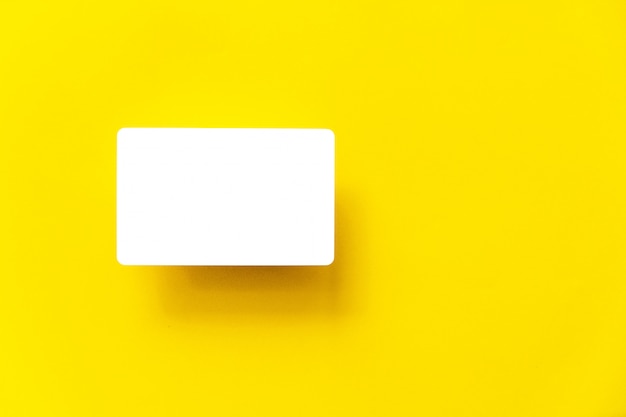 Draufsicht der leeren weißen Visitenkarte mit Schatten auf dem gelben Papierhintergrund.