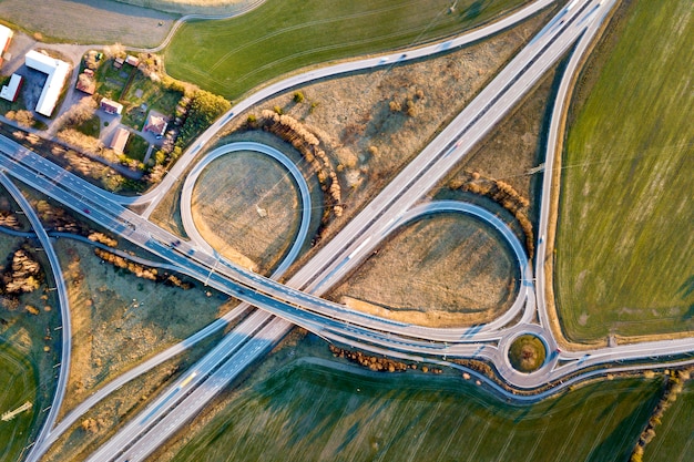 Draufsicht der Luft der modernen Landstraßenstraßenkreuzung, Hausdächer auf Frühlingsgrünfeld