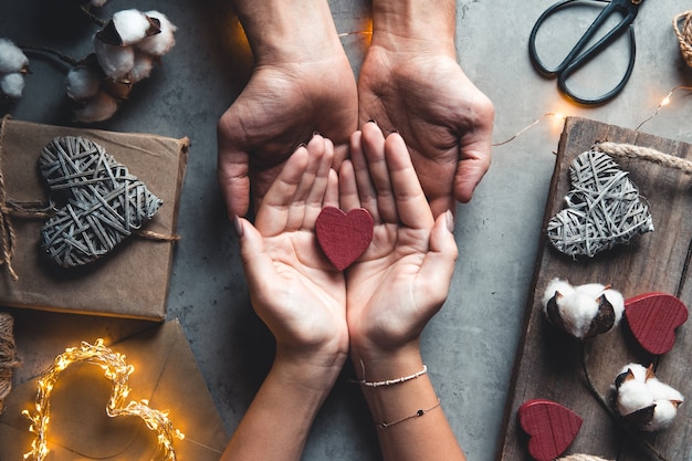 Draufsicht der männlichen und weiblichen Hände, die rote Geschenkbox mit goldenem Band halten