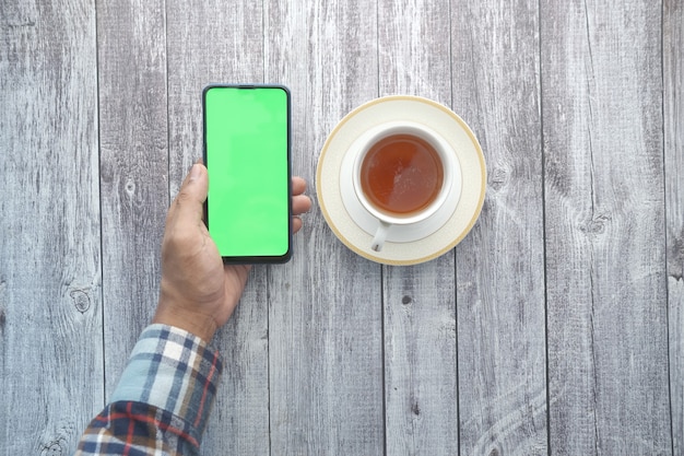Draufsicht der Mannhand, die Smartphone hält und Tee trinkt