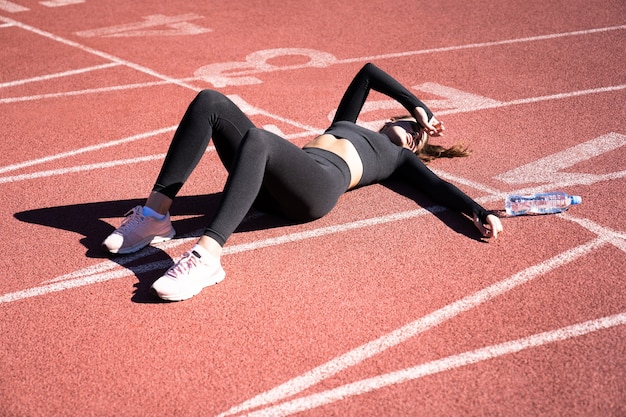 Draufsicht der müden fit Frau in Sportbekleidung, die nach dem Training oder Laufen auf einem Laufbandgummistadion ruht