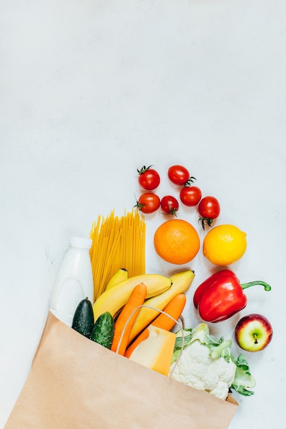 Draufsicht der Papiertüte mit Obst, Gemüse, Spaghetti, Käse, Milch auf weißer Oberfläche