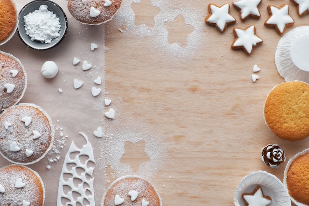 Draufsicht der Tabelle mit Zucker besprühten Muffins, Fondantzuckerglasur und Weihnachtssternplätzchen auf hellem Holz