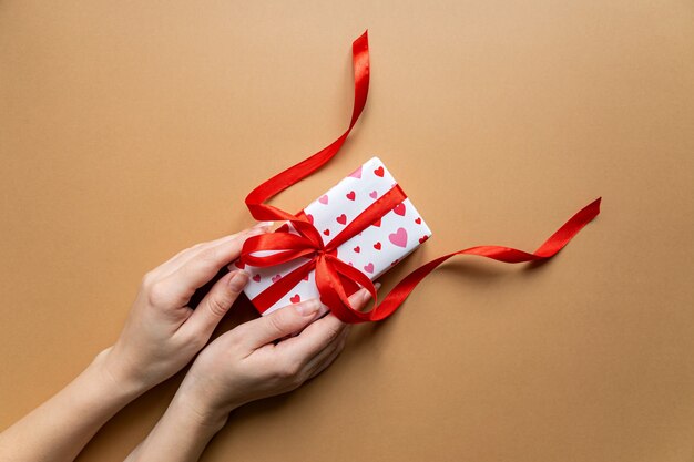 Draufsicht der weiblichen hände, die geschenkboxpaket über flachem laienhintergrund halten.