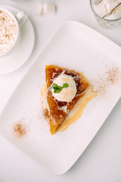 Draufsicht des Apfelkuchens mit geschmolzener Vanilleeiscreme auf der weißen Platte im Café