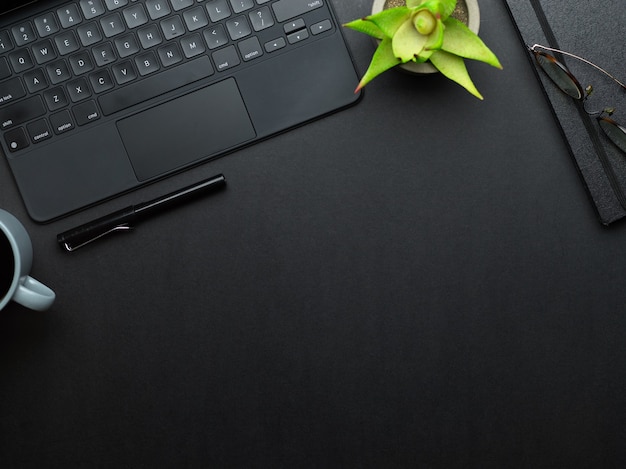 Draufsicht des Arbeitstisches mit Laptop-Tastatur, Stift, Notizbuch, Blumentopf und Kopierraum im Arbeitszimmer zu Hause