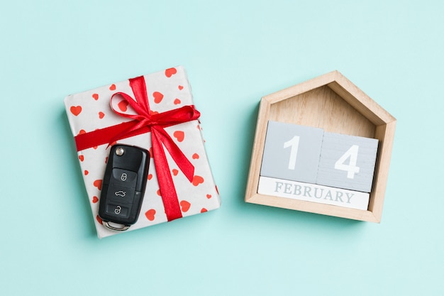 Draufsicht des Autoschlüssels auf einer Geschenkbox mit roten Herzen und festlichem Kalender auf buntem. 14. Februar. Geschenk zum Valentinstag