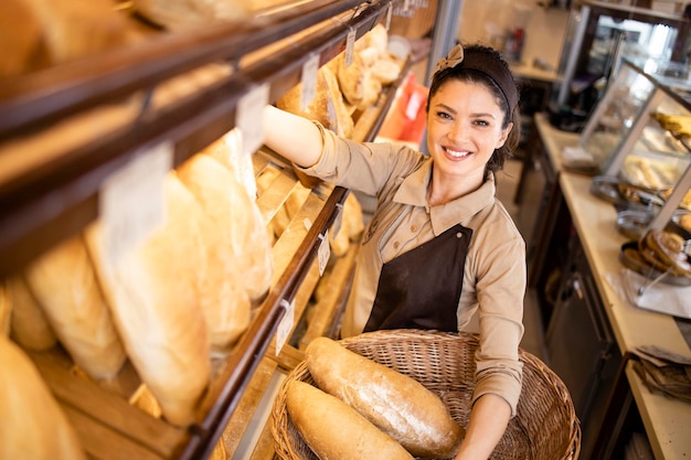 Draufsicht des Bäckereiverkäufers, der frisches Brot in Regalen in der Bäckerei arrangiert
