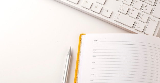 Draufsicht des Bürotisch-Schreibtischkonzeptes mit Tastatur, Notizbuchplanung, Bleistift auf dem weißen Hintergrund.