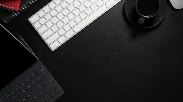 Draufsicht des dunklen modernen Arbeitsplatzes mit digitalem Tablett, Computertastatur, Kaffeetasse